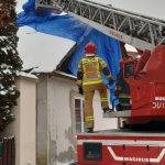 Strażacy zabezpieczają plandeką dach na budynku mieszkalnym.