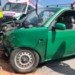 Rozbity zielony samochod w tle ambulans pogotowia ratunkowego.