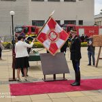 Starosta Puławski trzyma w rękach Sztandar w tle samochody strażackie.