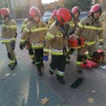 Strażacy przenoszą poszkodowanego na desce ortopedycznej.