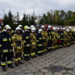 Strażacy ochotnicy stoją w szeregu na placu wewnętrznym Komendy Powiatowej Państwowej Straży Pożarnej w Puławach.