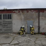 Dwóch strażaków ochotników podczas ćwiczeń na tle budynku.