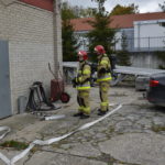 Dwóch strażaków podczas ćwiczeń na tle budynku.