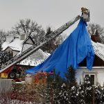Strażacy zabezpieczają plandeką dach na budynku mieszkalnym.