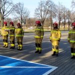 Dowódca jednostki ratowniczo gaśniczej oraz strażacy stoją przed budynkiem Komendy.